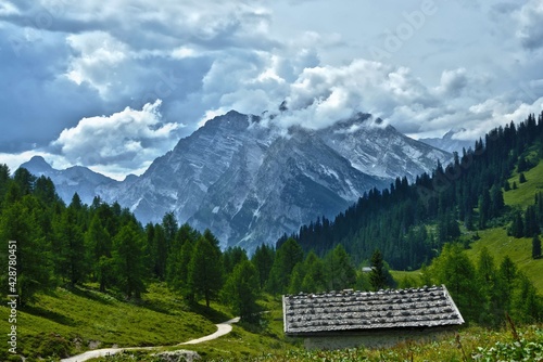 alpine hut on pasture in front of wood and mountains with clouds