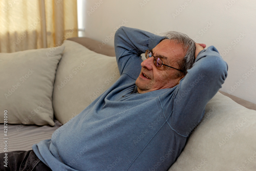Senior man relaxing at home and thinking with hands behind head. Mature man wearing eyeglasses while resting at home and looking away. Senior man enjoy weekend leisure time at home. Copy space.