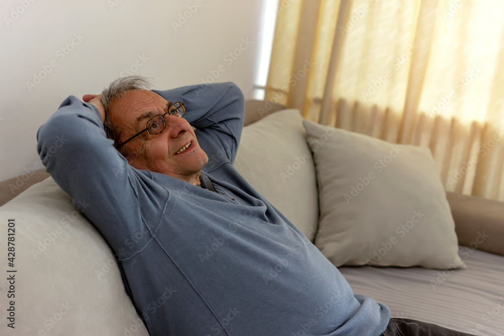 Peaceful older man feel relax on comfortable sofa in living room, calm mature male rest on cozy sofa, enjoy weekend at home. Side view of a 70s man with hands behind head enjoy at home, leaned on sofa