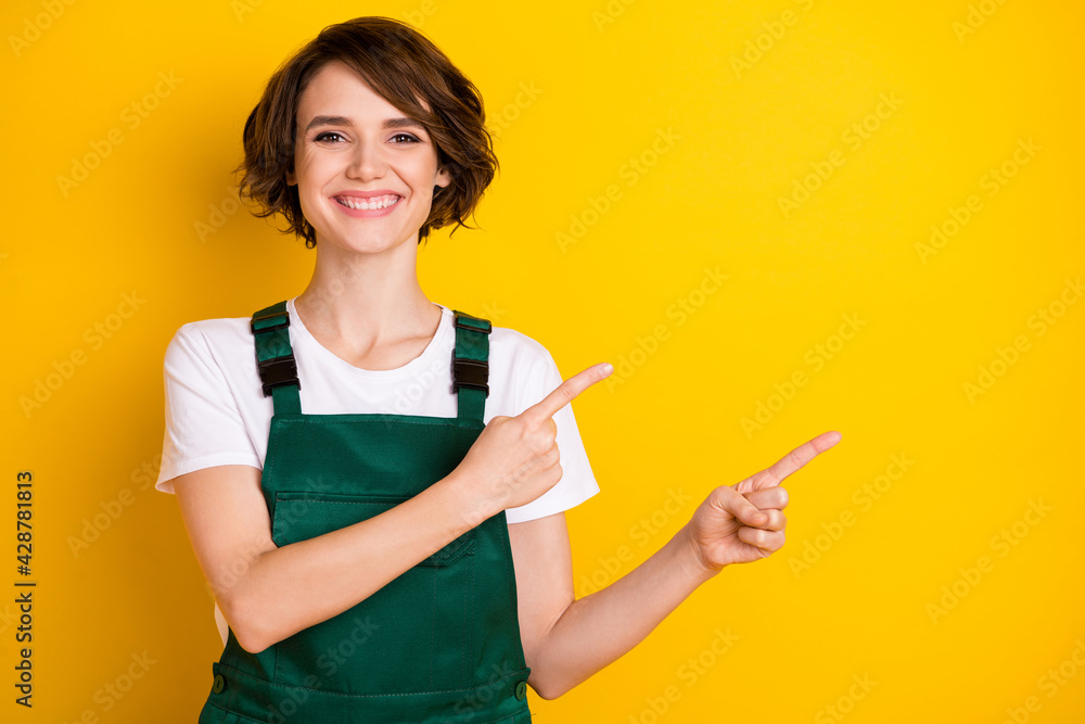 Portrait of pretty cheerful person beaming smile indicate fingers empty space isolated on yellow color background Portrait of pretty cheerful person beaming smile indicate fingers empty space isolated on yellow color background