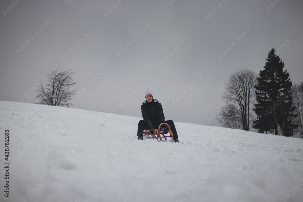 Teenager caught riding on a wooden sledge trying to adjust his direction with his hand and concentrating on his ride. In winter, the athlete goes down the piste on a historical object. Czech republic