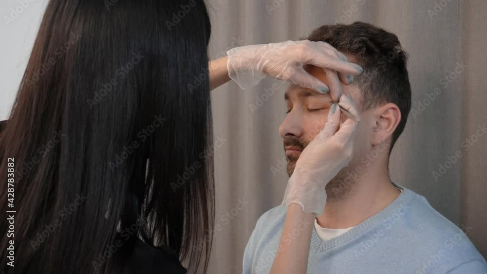 Stylist plucking eyebrows with tweezers. Handsome attractive male face of a middle aged man. Eyebrow styling and care Stylist plucking eyebrows with tweezers. Handsome attractive male face of a middle aged man. Eyebrow styling and care