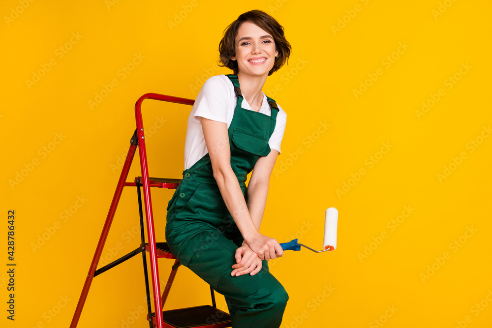 Fototapeta premium Photo of happy cheerful girl painter sit ladder relaxing from work holding roller break pause isolated on yellow color background