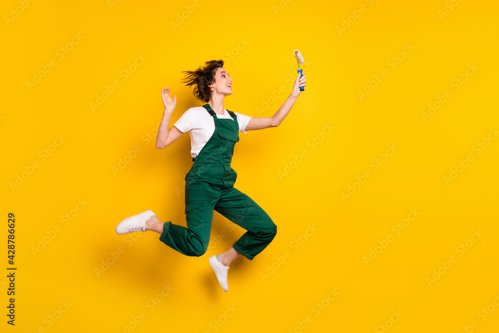 Full size photo of happy smiling excited crazy woman painter jumping looking at roller isolated on yellow color background