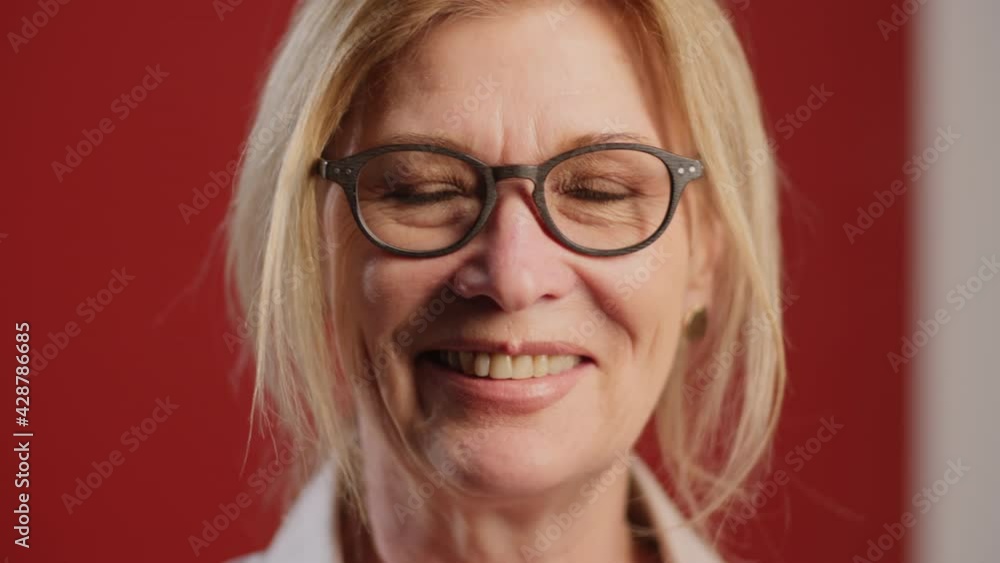 Close up portrait shot of beautiful senior woman with blonde hair smiling at camera while posing on red background Close up portrait shot of beautiful senior woman with blonde hair smiling at camera while posing on red background