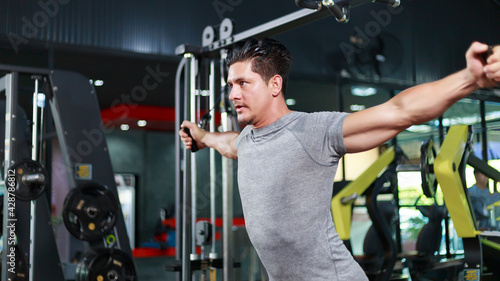 Young attractive strong Caucasian man in sportswear concentrate lifting cable exercising chest muscles in a modern fitness club. Sport and exercise concept
