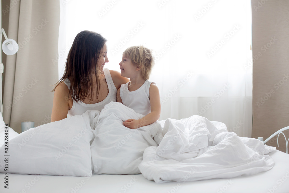 Beautiful blond child and his mother, playing at home in the morning in bed, smiling, laughing and having fun Beautiful blond child and his mother, playing at home in the morning in bed, smiling, laughing and having fun