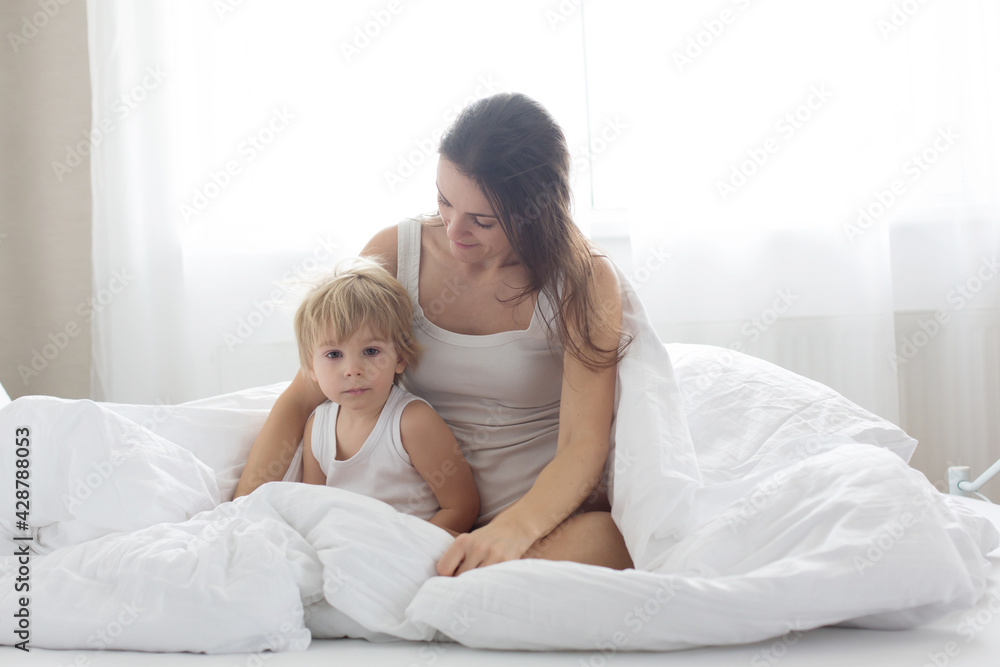 Beautiful blond child and his mother, playing at home in the morning in bed, smiling, laughing and having fun Beautiful blond child and his mother, playing at home in the morning in bed, smiling, laughing and having fun
