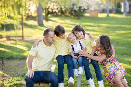 Beautiful family, mother, father and three kids, boys, having familly outdoors portrait taken on a sunny spring evening, beautiful blooming garden, sunset time