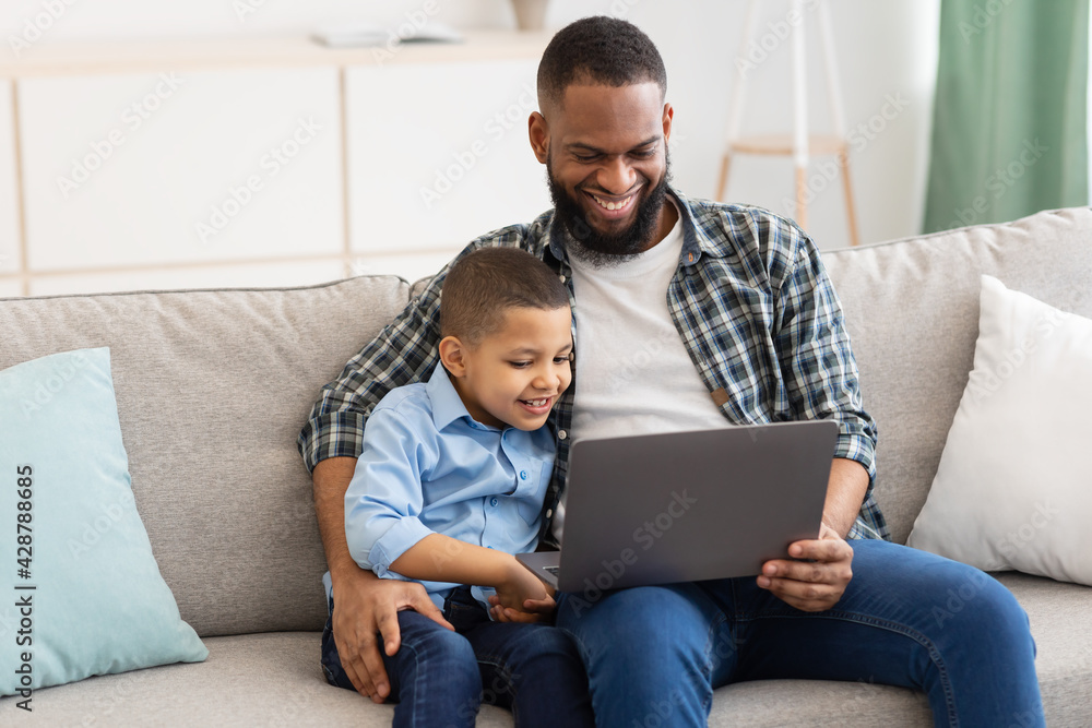 African Daddy Embracing Son Sitting With Laptop Watching Cartoons Indoor African Daddy Embracing Son Sitting With Laptop Watching Cartoons Indoor