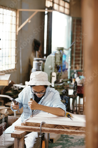 Professional carpenter with chisel and hammer carving wood board when making furniture item for customer