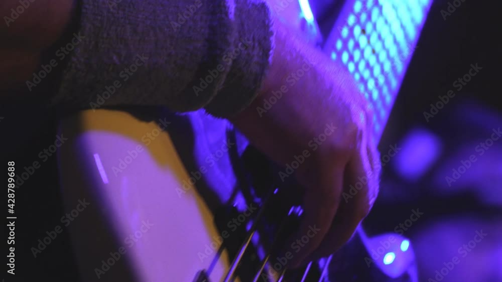The bass player plays a white five-string bass guitar. Selective focus The bass player plays a white five-string bass guitar. Selective focus
