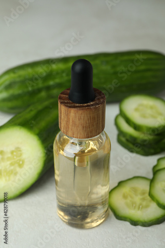 Bottle of cosmetic oil and cucumbers on white textured background