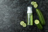 Bottle with cosmetics and cucumber on black smokey background