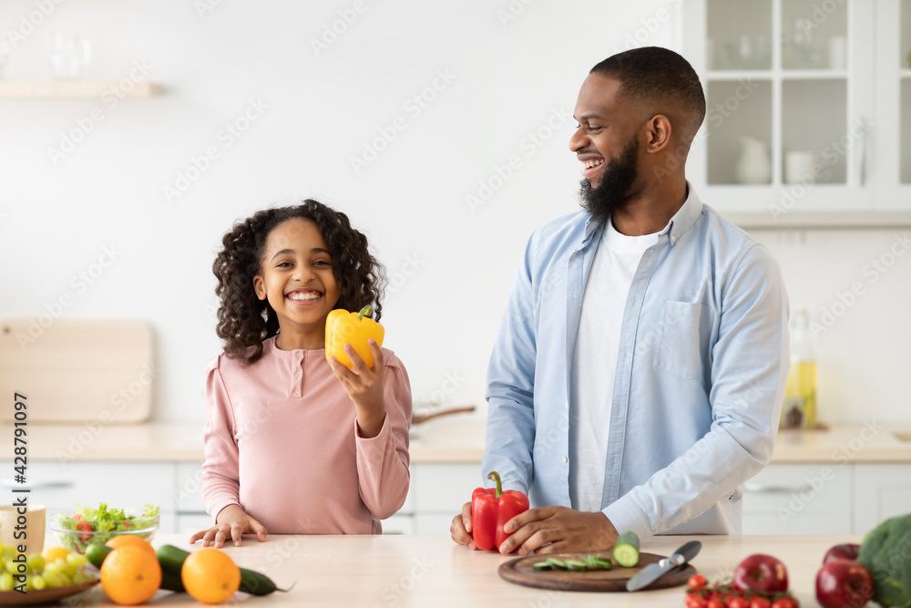 Cheerful african father and daughter cooking healthy salad