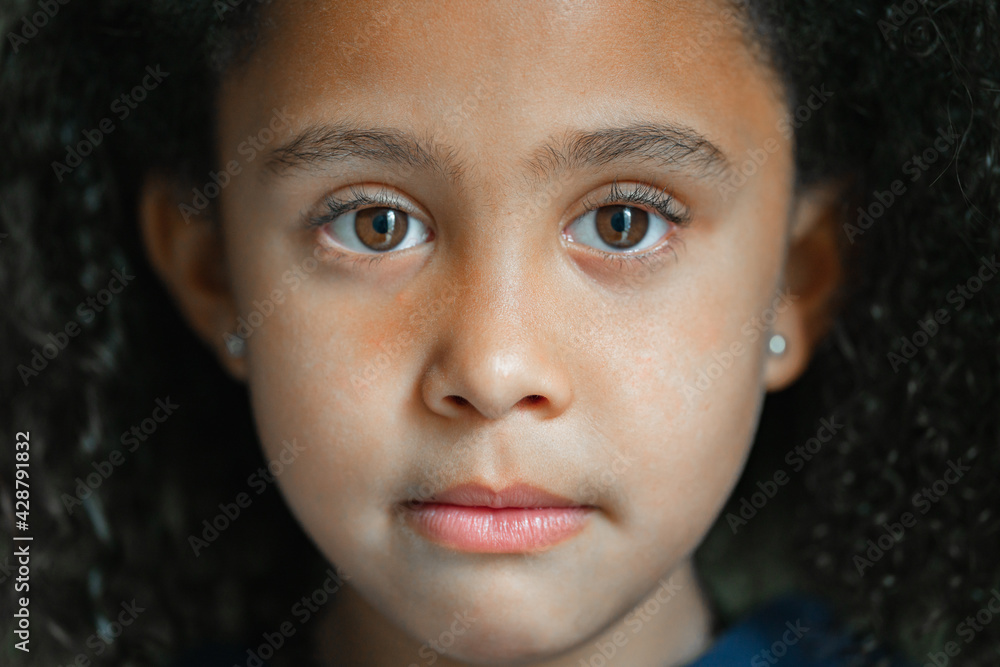 Close up of afro little girl sad looking at camera with brown eyes and curly hair Close up of afro little girl sad looking at camera with brown eyes and curly hair