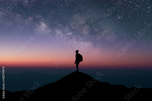 Silhouette of young traveler and backpack watched the star and milky way alone on top of the mountain with beautiful night sky. He enjoyed traveling and was successful when he reached the summit.