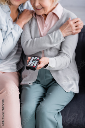 Cropped view of remote controller in hand of mature woman near daughter