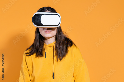 young woman with a virtual reality device on a yellow background. © Alexander