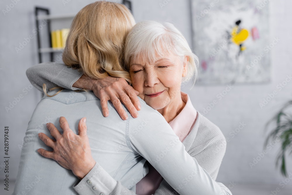 Grey haired woman hugging daughter at home Grey haired woman hugging daughter at home