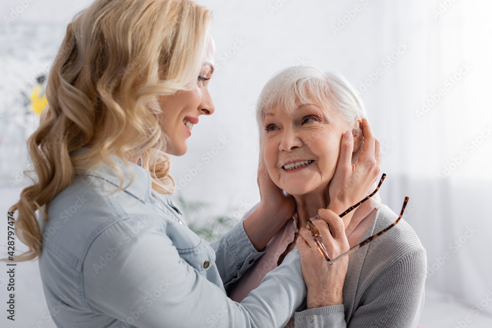 Smiling woman touching face of senior mother with eyeglasses Smiling woman touching face of senior mother with eyeglasses
