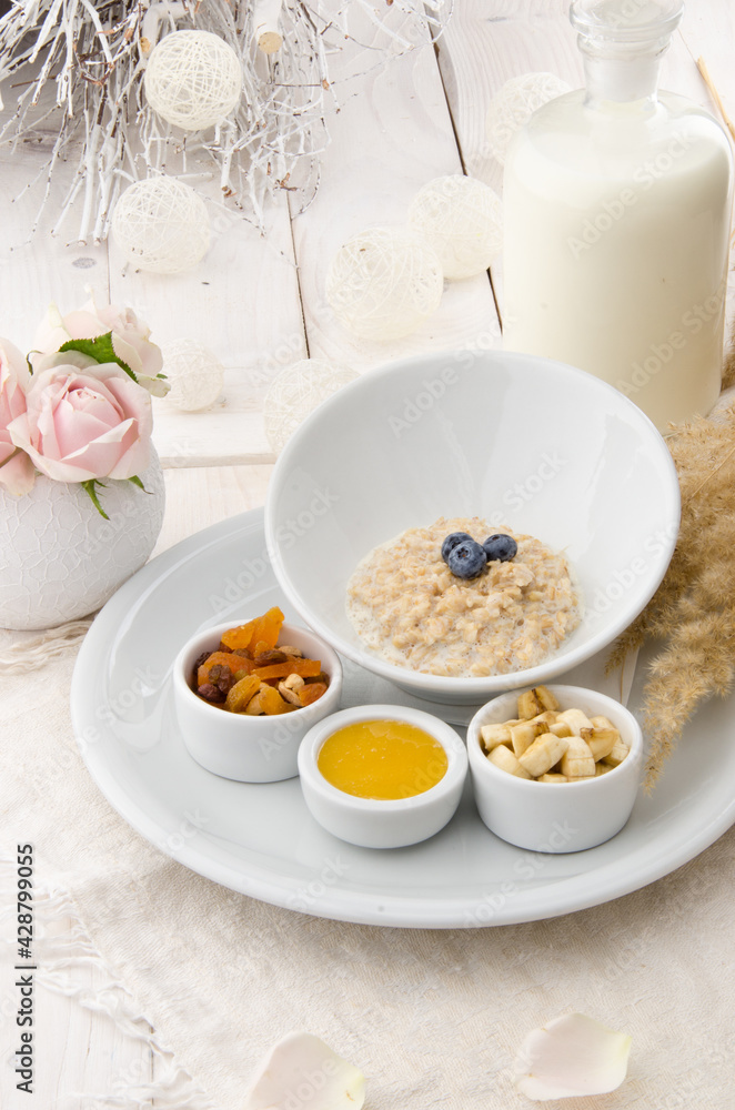 Oatmeal with blueberries in a beautiful white plate with honey, berries and a banana on a light delicate background. Healthy breakfast. Oatmeal with blueberries in a beautiful white plate with honey, berries and a banana on a light delicate background. Healthy breakfast.