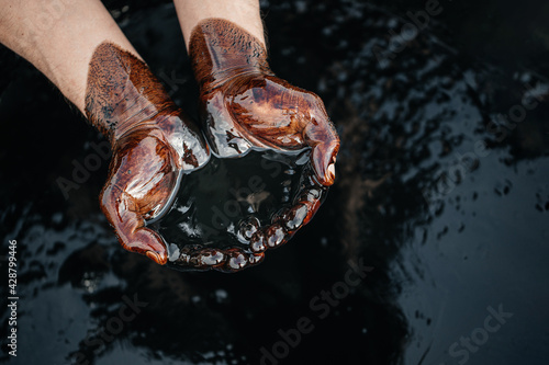 Foto Hands are soaked in crude oil against the background of spilled petroleum products
