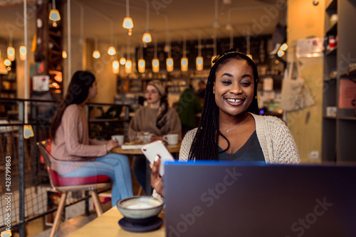 Portrait of young woman working on using laptop at coffee shop.
