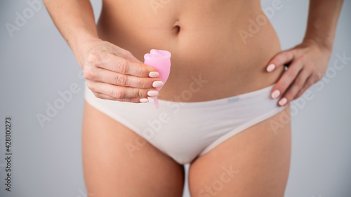 A faceless woman in white panties holds a folded menstrual cup on a white background