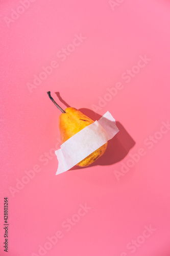 A ripe pear is glued with white tape to a pink background. Creative fun concept in the style of minimalism.