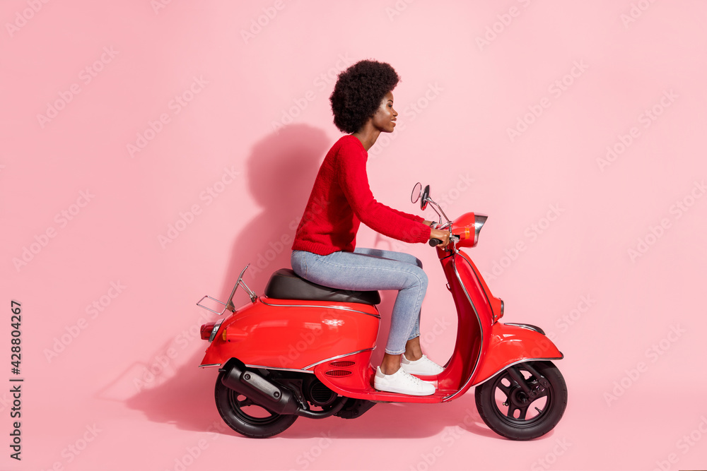 Full size profile side photo afro american pretty woman ride motorcycle isolated on pastel pink color background Full size profile side photo afro american pretty woman ride motorcycle isolated on pastel pink color background