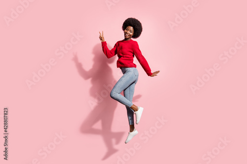Full length body size view of attractive cheerful girl jumping showing v-sign having fun isolated over pink pastel color background
