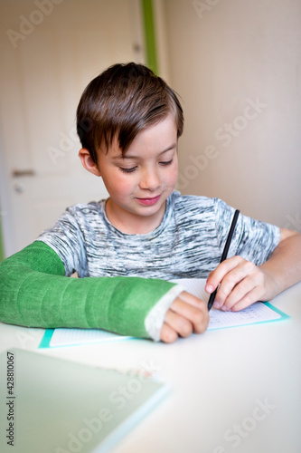 cool boy with green arm cast is sitting in his room and is writing something and is doing housework