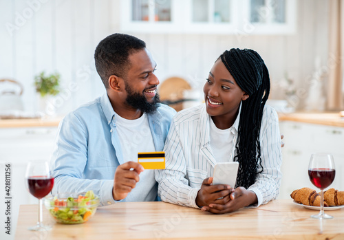 Black Couple Ordering Food Online With Smartphone And Credit Card In Kitchen