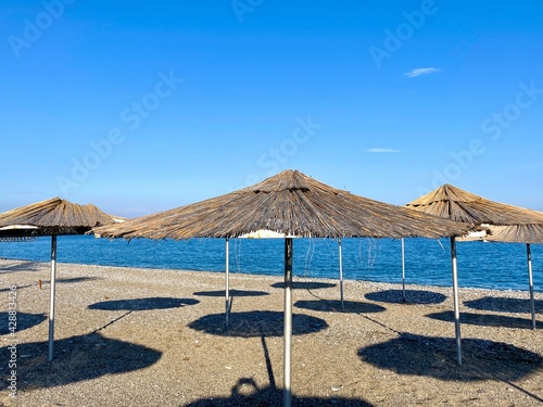 Fototapeta Naklejka Na Ścianę i Meble -  Empty beach with reed umbrellas, no one on the beach.  Beautiful blue sky, sea, sand, hot weather.  A beach without travelers and tourists.  Quarantine due to covid-19 coronavirus.