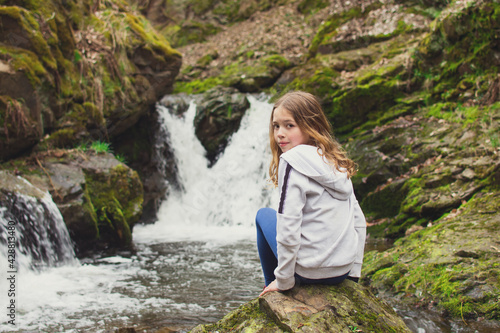 Young girl sitting on the rock and looking at waterfall on the river in the rocks. Tourism with children concept.