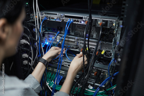 Close up of female network technician connecting cables in server cabinet while setting up supercomputer at data center, copy space