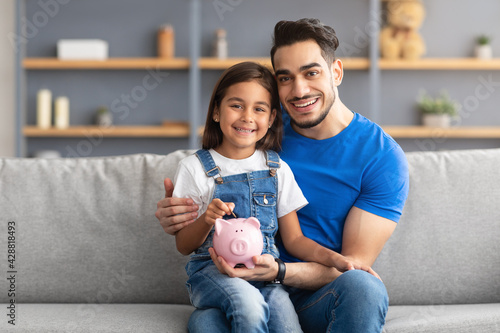 Foto Little girl and dad saving money in piggy bank