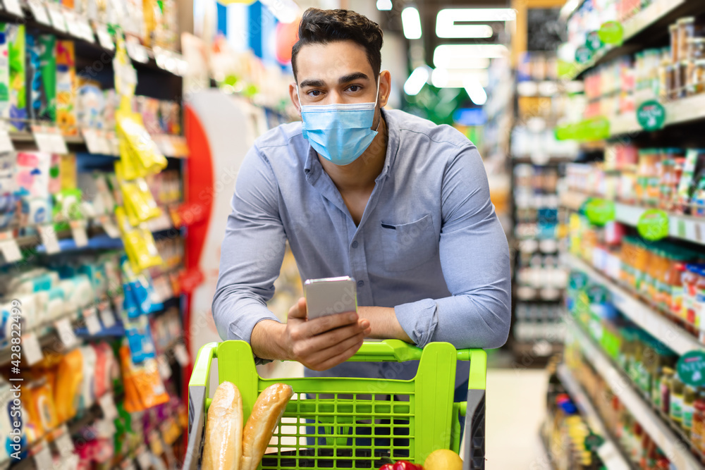 Arabic Male Customer With Smartphone Doing Grocery Shopping In Supermarket