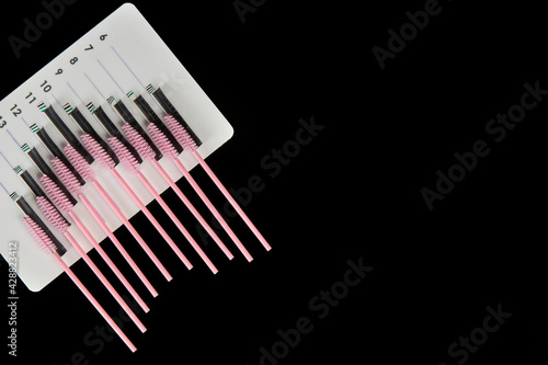 A tablet with false eyelashes and brushes on a black background. Cosmetic accessories for eyelash extensions