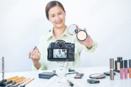 Woman making a video for her blog on cosmetics using digital camera. Young female blogger on camera screen holding cosmetics.