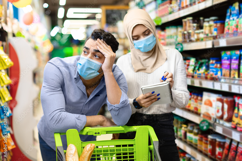 Unhappy Muslim Couple Calculating Prices Doing Grocery Shopping In Supermarket