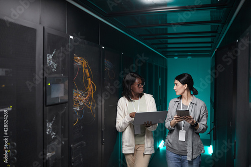 Vászonkép Portrait of two young women using laptop in server room while setting up superco