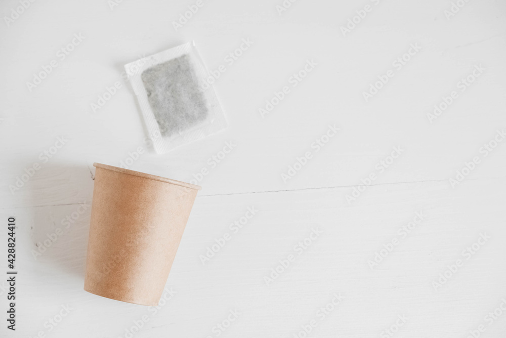 Obraz premium Paper cup and square dry tea bag on a white background. Top view. Copy, empty space for text