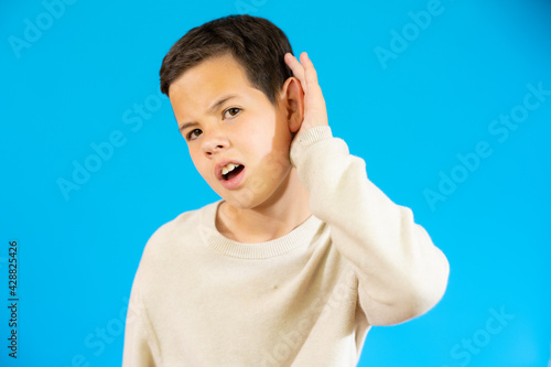 Little child making listening gesture isolated over blue background.