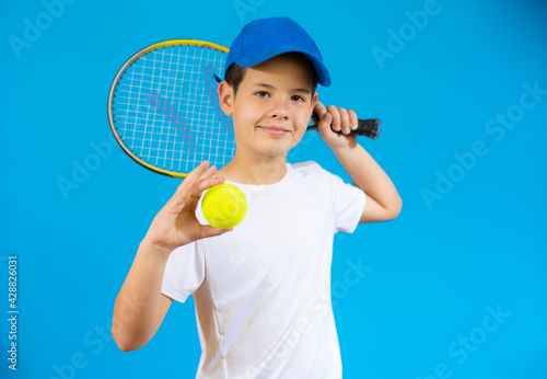Young boy with tennis racket and ball isolated over blue background. © Danko