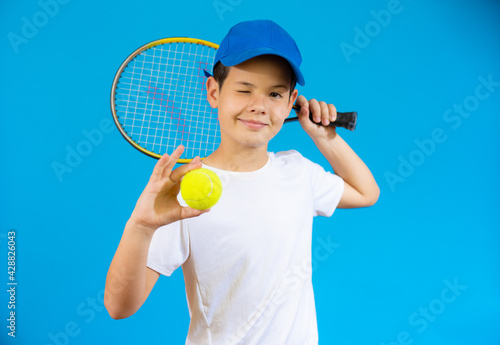 Young boy with tennis racket and ball isolated over blue background. © Danko