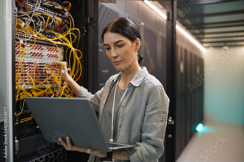 Waist up portrait of female network engineer connecting cables in server cabinet while working with supercomputer in data center, copy space photo