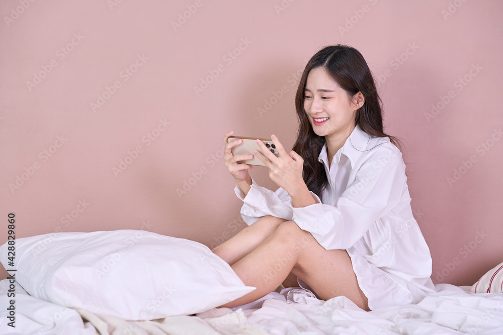 sexy woman in white shirt Laughing and touching a smartphone on bed sexy woman in white shirt Laughing and touching a smartphone on bed