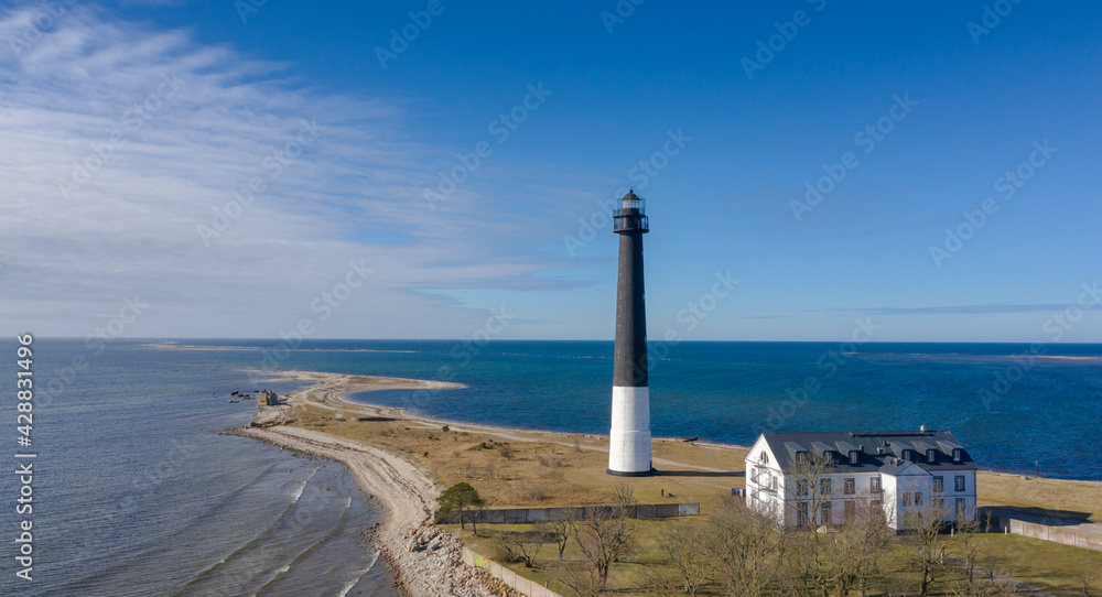 Obraz premium Aerial view to the historic lighthouse on on the daytime seascape with the long spit submerging into deep blue sea